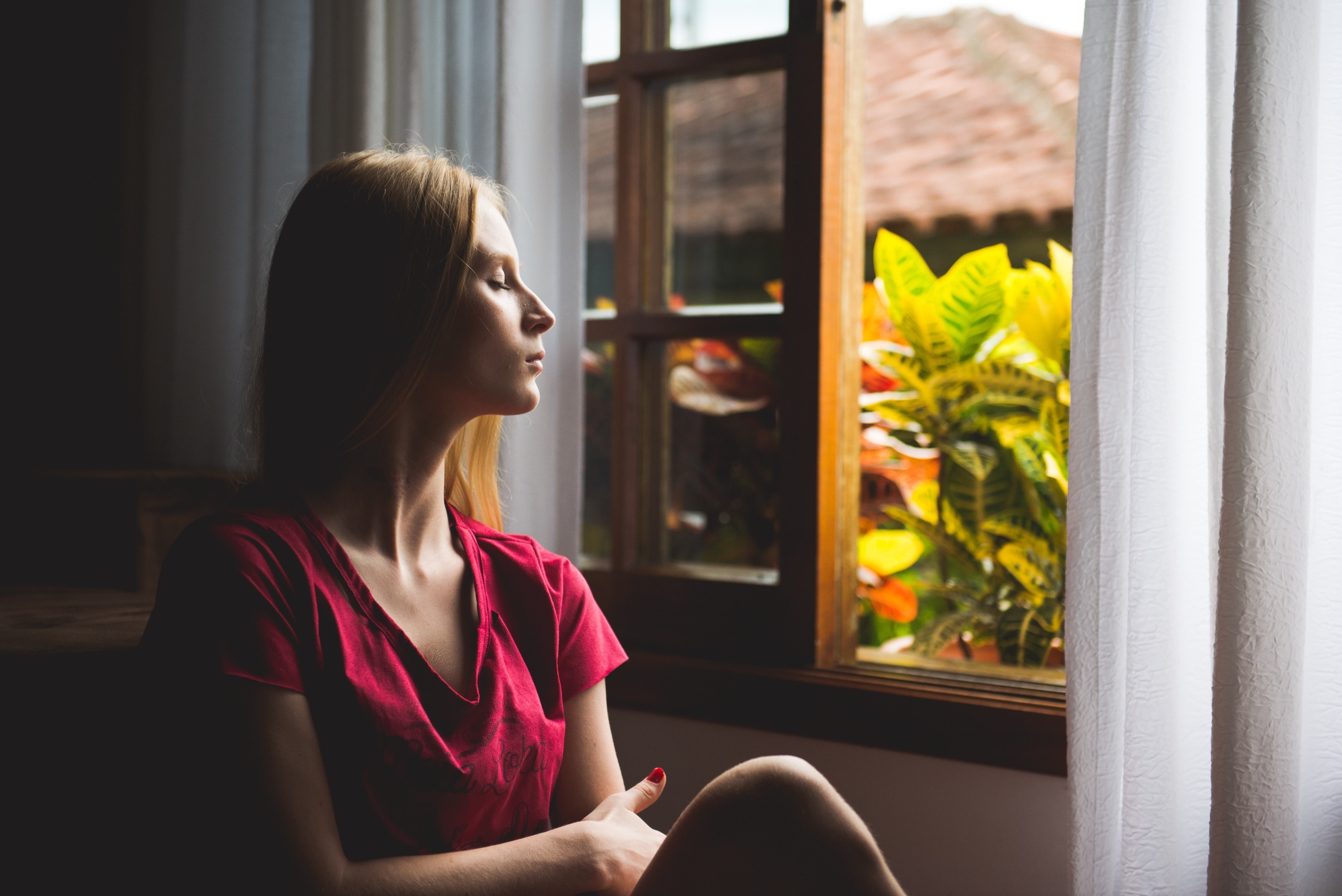 lady with closed eyes next to a window